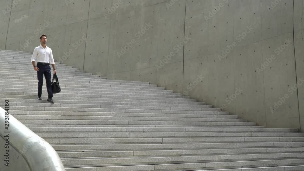 Mid shot of handsome and fit European man with dark hair in white collared shirt and dark trousers is walking down a grand modern concrete staircase towards camera and out of frame Mid shot of handsome and fit European man with dark hair in white collared shirt and dark trousers is walking down a grand modern concrete staircase towards camera and out of frame