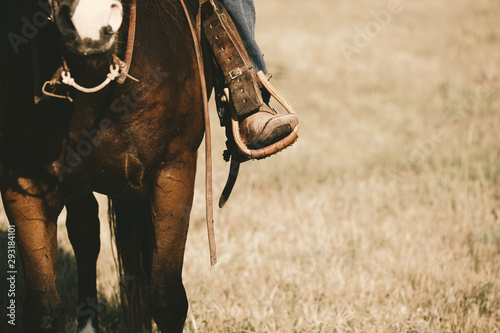 Western lifestyle shows boot in stirrup close up on horse during horseback riding, copy space on field background. photo