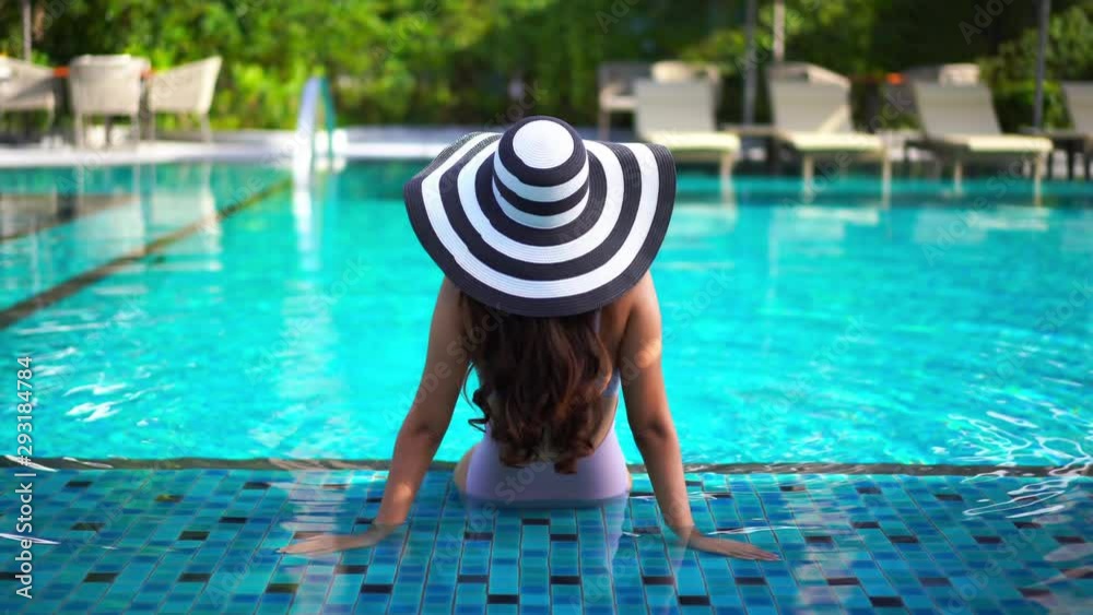 Woman sitting in the swimming pool with her back to the camera wearing ...