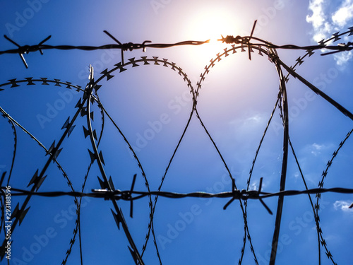 Steel rolled barbed wire on sunny blue sky with sun flare background