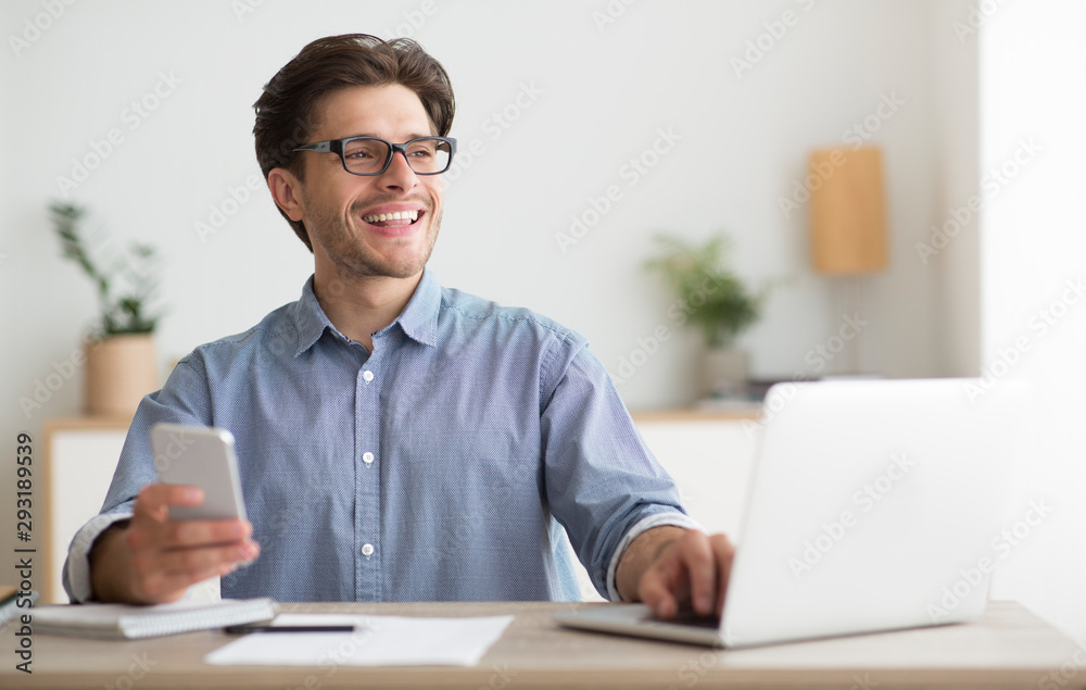 Man Using Smartphone Sitting In Front Of Laptop In Office Man Using Smartphone Sitting In Front Of Laptop In Office