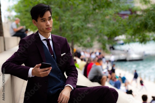 Young Businessman sitting on riverwalk holding his mobile phone, Chicago, Illinois, United States photo