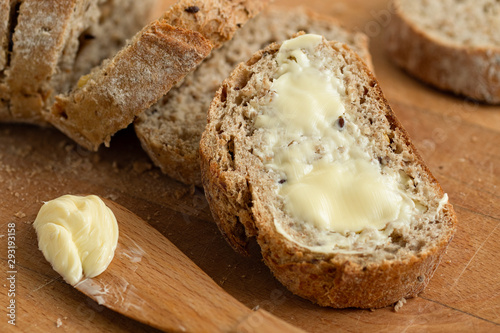 Vászonkép Closeup of buttered slice of whole wheat rustic bread next to cut bread and wood knife