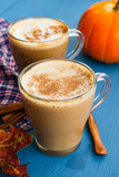 Pumpkin spiced coffee with milk and cinnamon in a glass mug. Autumn or winter hot drink on a blue wooden table. Close up