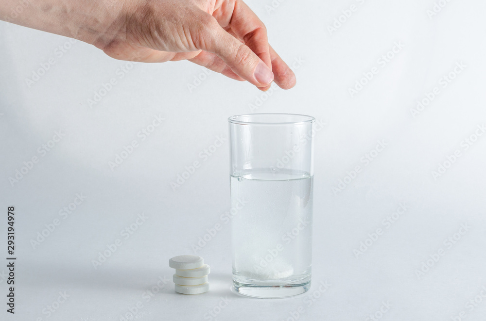 A hand holds an effervescent soluble tablet and places it in a glass of water. Isolated on white background. The concept of treatment and prevention of viral diseases. Help for depression and insomnia A hand holds an effervescent soluble tablet and places it in a glass of water. Isolated on white background. The concept of treatment and prevention of viral diseases. Help for depression and insomnia