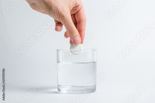 A hand holds an effervescent soluble tablet and places it in a glass of water. Isolated on white background. The concept of treatment and prevention of viral diseases. Help for depression and insomnia