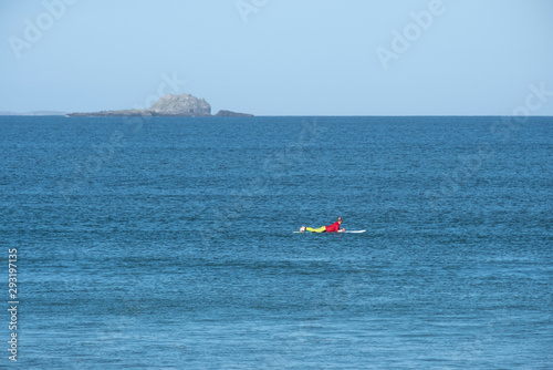 Surfer on the board waiting for the wave in the ocean with lone island in the background from distance 