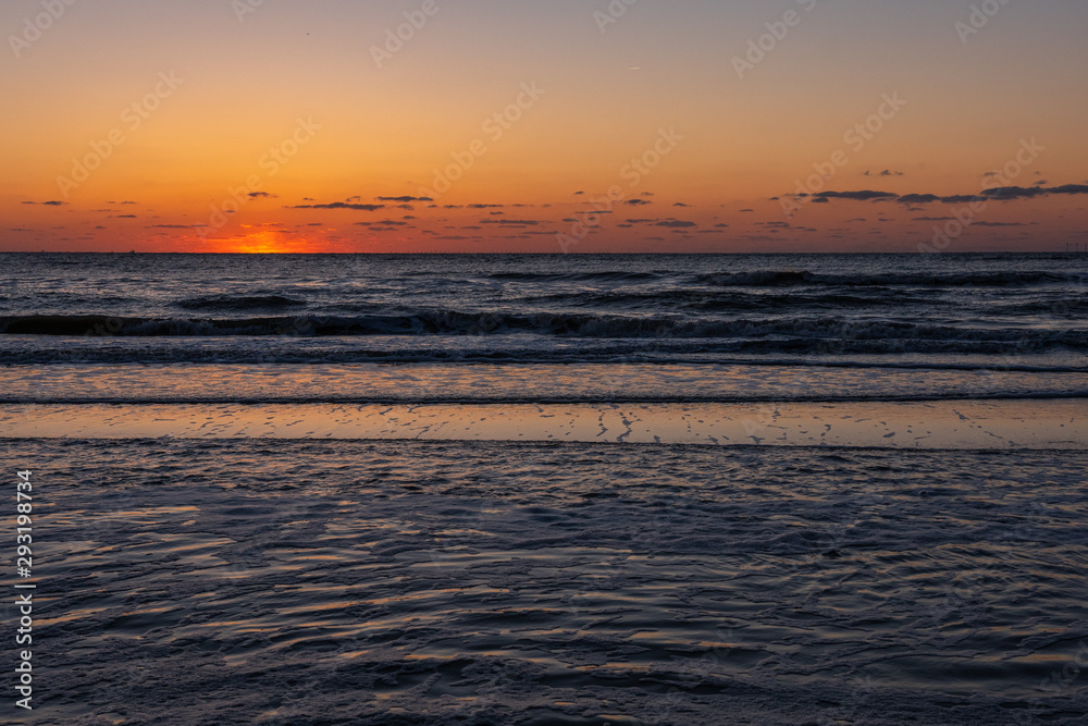 Amazing sunset view on the beach. Beautiful sunset landscape at the North sea and orange sky above it with awesome sun golden reflection on waves as a background.
