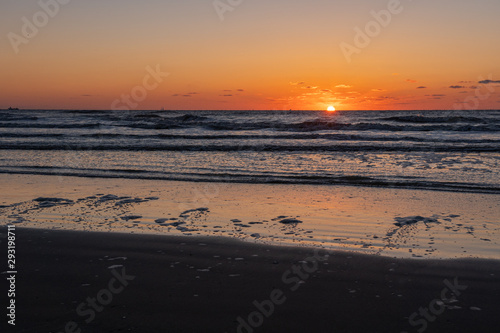 Beautiful sunset landscape at the North sea and orange sky above it with awesome sun golden reflection on waves as a background. Amazing summer sunset view on the beach.