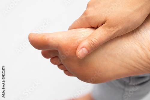 A closeup view on the foot of a person with a busy lifestyle  tired and aching  using hand to rub the underside of the sole and big toe  isolated against a white background.