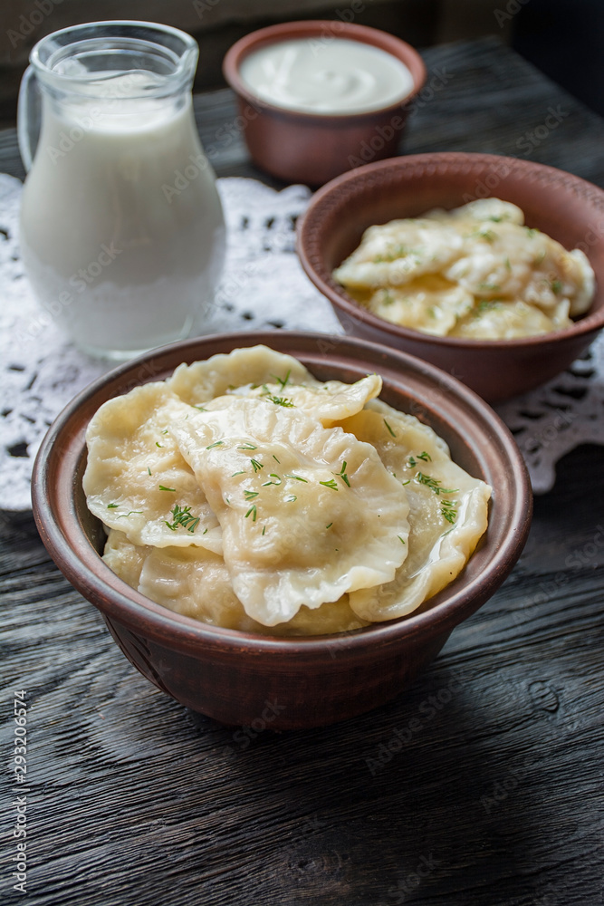 Dumplings with potatoes and cabbage. Sour cream, milk and greens. Traditional dish of Ukraine. Dark wooden background. Dumplings with potatoes and cabbage. Sour cream, milk and greens. Traditional dish of Ukraine. Dark wooden background.