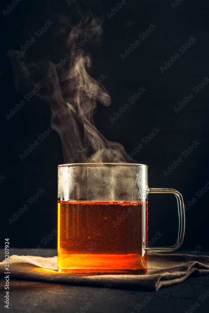 Black hot tea in clear glass Cup, steam coming out of mug on black