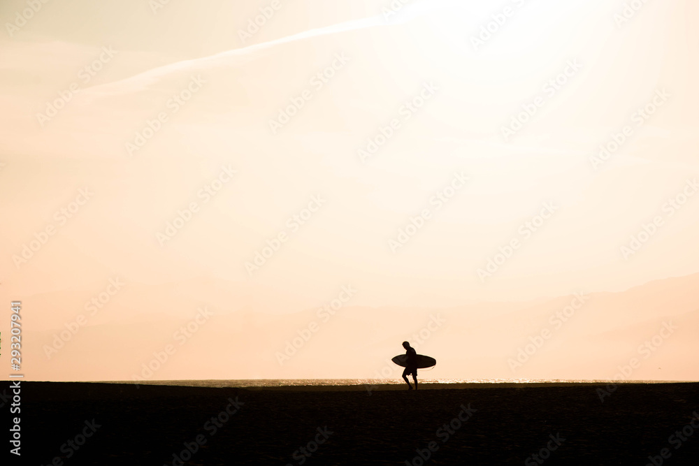 Silhouette of a surfer walking to the sea at sunset. Surfer at santa monica beach los angeles california united states