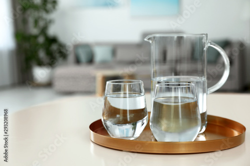 Tray with jug and glasses of water on white table in room, space for text. Refreshing drink
