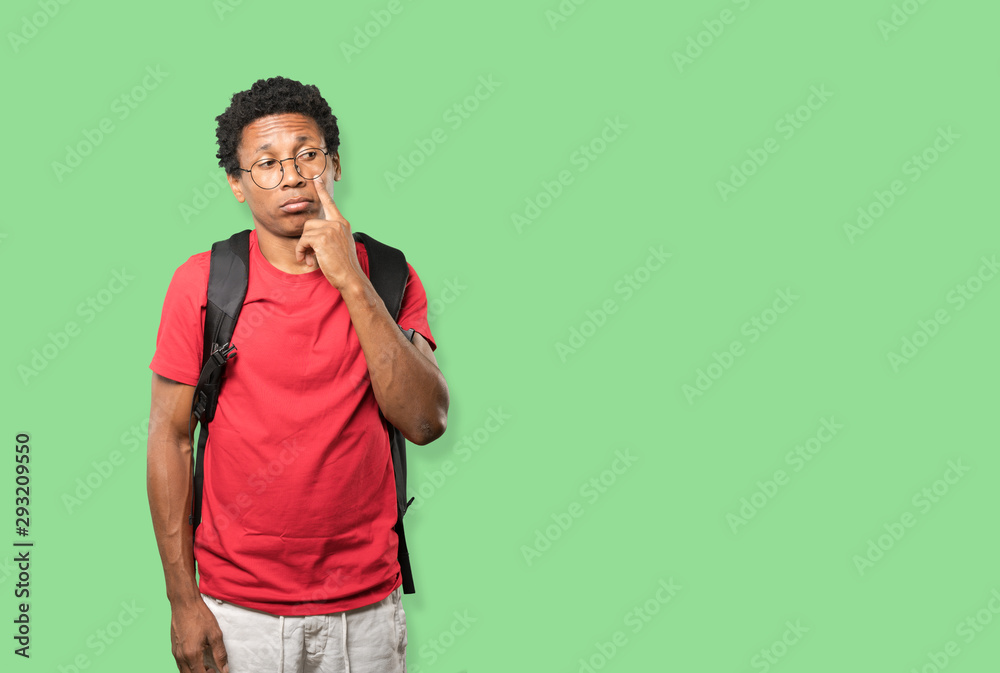 Hesitant young man making a gesture of being careful with his hand pointing at his eye Hesitant young man making a gesture of being careful with his hand pointing at his eye