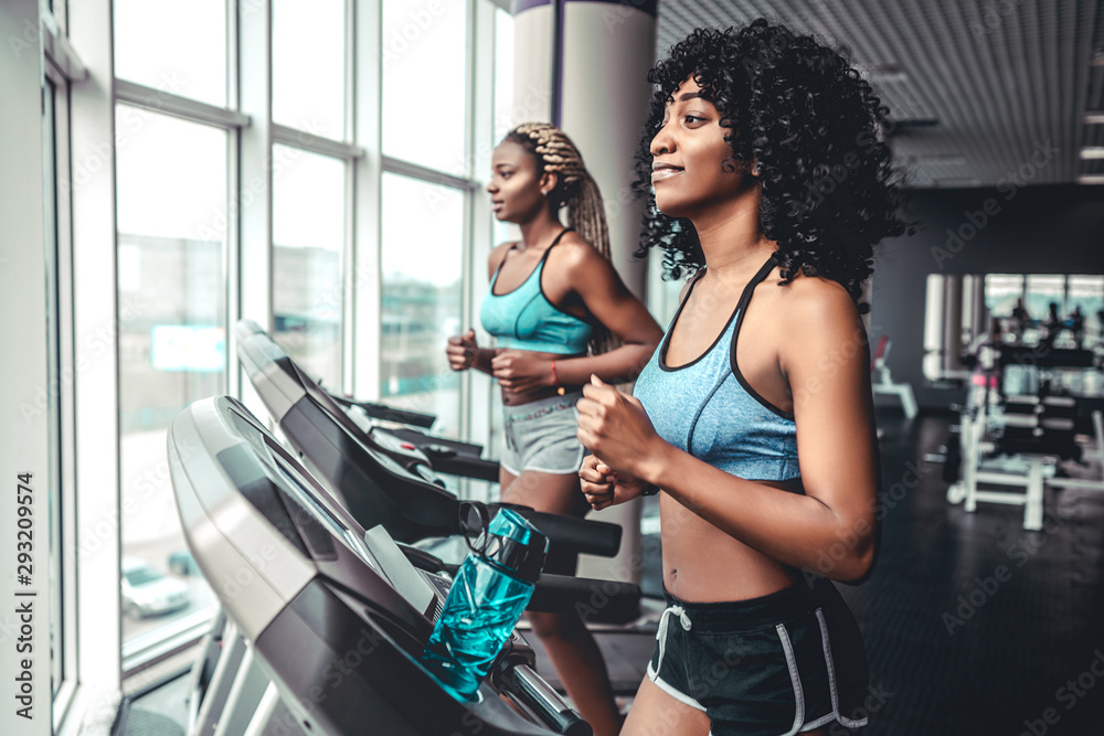 Side view of two attractive sports women on running track. Girls on treadmill Side view of two attractive sports women on running track. Girls on treadmill