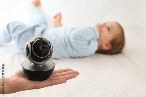 Woman holding baby camera near child on bed. Video nanny