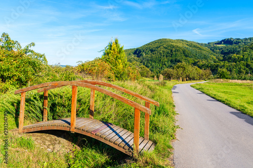Small wooden footbridge on Velo Dunajec cycling path and green rural landscape near Nowy Sacz, Poland