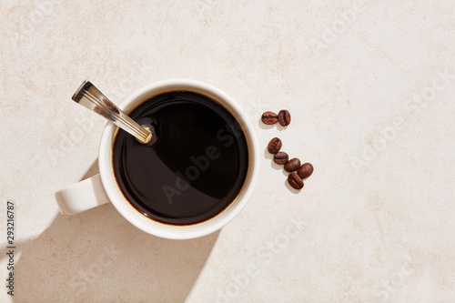 Dark black coffee in a white mug with coffee beans under harsh summer sunlight