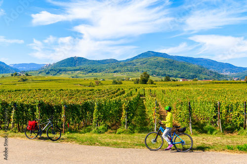Young woman cyclist stopping by vineyards on Alsatian Wine Route near Ribeauville village, France