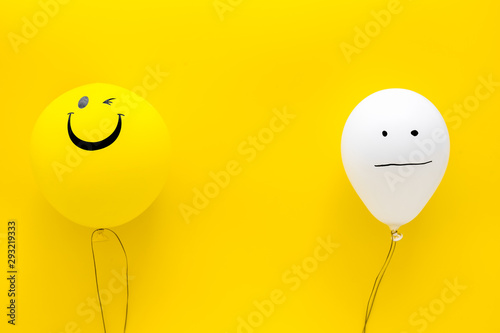 Treat depression concept. Balloons with frustrated and smiling faces on yellow background top view copy space