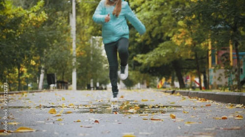 Girl play and jump in puddle in park after autumn rain. Fall rainy weather outdoors activity for young child. Kid jumping in muddy puddles. Slow motiom 180 FPS. photo