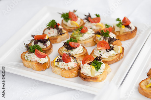Close-up of wedding reception with tasty sandwiches and canapes made of sausage, parsley and tomatoes with cream cheese. Canapes on white ceramic plates at wedding reception.