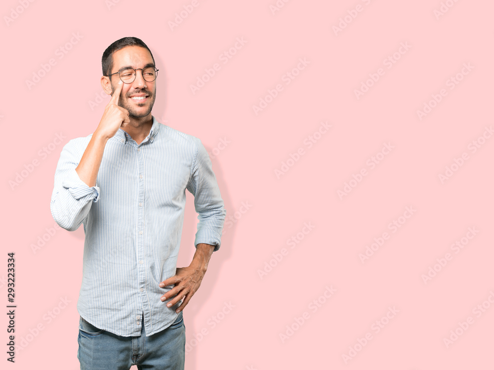 Friendly young man making a gesture of being careful with his hand pointing at his eye Friendly young man making a gesture of being careful with his hand pointing at his eye