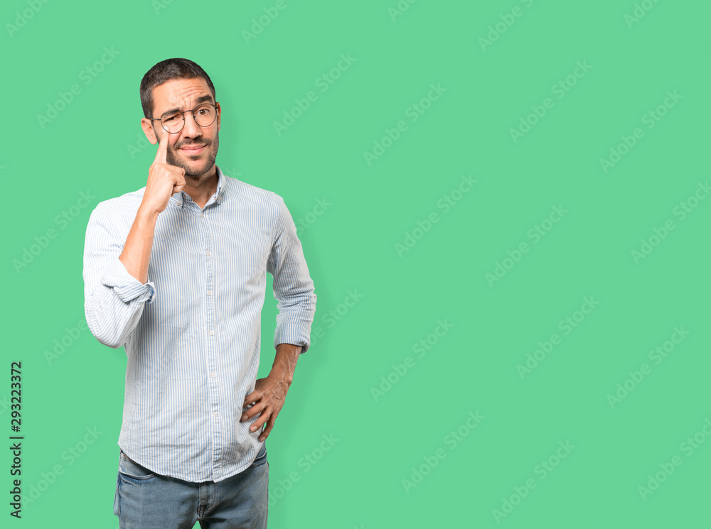 Hesitant young man making a gesture of being careful with his hand pointing at his eye Hesitant young man making a gesture of being careful with his hand pointing at his eye