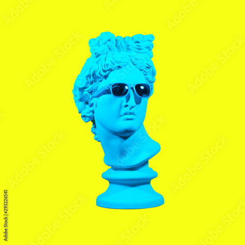 Statue on a yellow background. Gypsum statue of David's head. Creative. Plaster statue of Apollo's head in blue sunglasses. Minimal concept art.