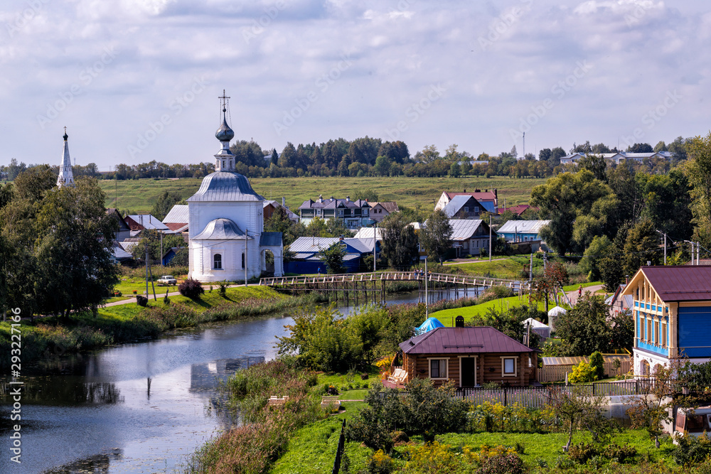 Idyllic Russian summer rural landscape with apartment buildings, church, river. Suzdal vastness, Russia.