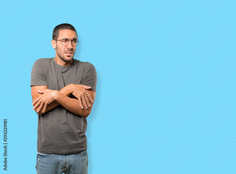 Concerned young man making a gesture of being cold Concerned young man making a gesture of being cold