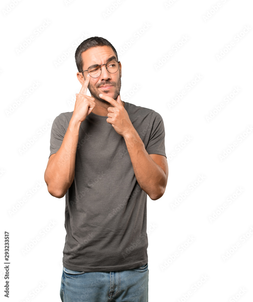 Hesitant young man making a gesture of being careful with his hand pointing at his eye Hesitant young man making a gesture of being careful with his hand pointing at his eye