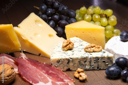 Assorted cheeses, nuts, grapes, fruits, smoked meat and a glass of wine on a serving table. Dark and Moody style.