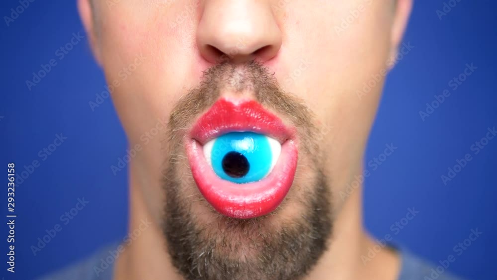close-up. A bearded man with painted lips holds a blue eye candy in his mouth. close-up. A bearded man with painted lips holds a blue eye candy in his mouth.