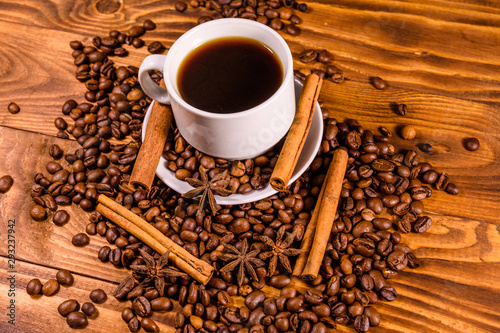Cup of hot coffee, star anise, cinnamon sticks and scattered coffee beans on wooden table