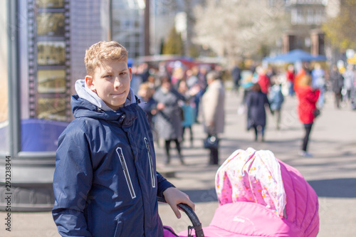 a teenager with blond hair walks with a child in a pram