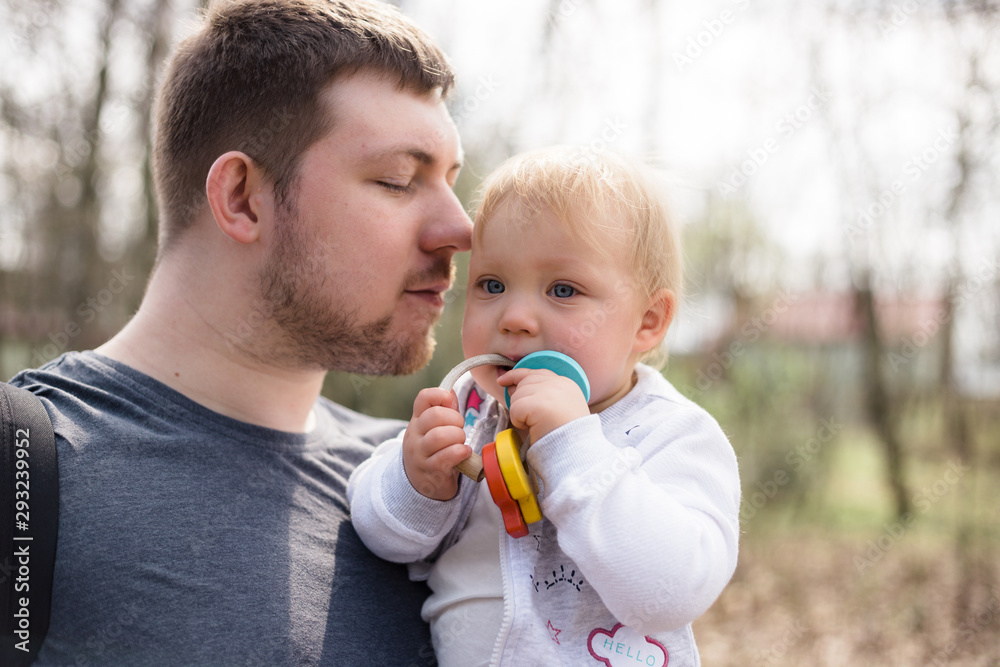 Young father holding his baby daughter while walking in a park in early spring. Young father holding his baby daughter while walking in a park in early spring.