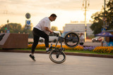 The guy performs a stunt on BMX, standing on the rear wheel.