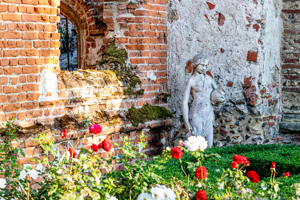 white sculpture next to old red brick wall covered with moss and roses are on foreground
