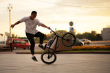 The guy jumps off the BMX, which is standing on the rear wheel.