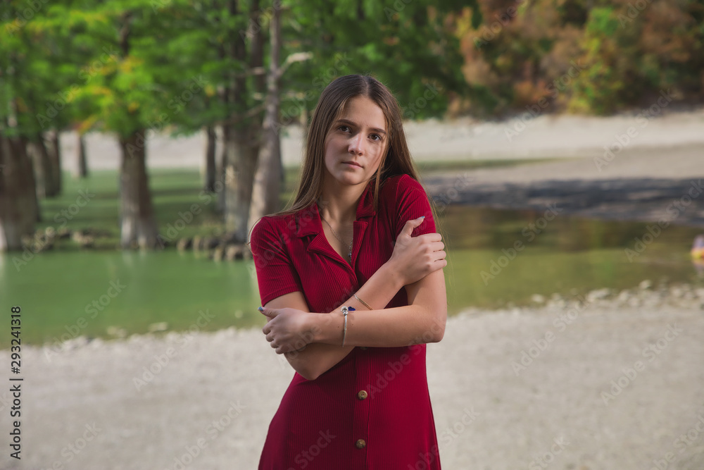 a beautiful, young brown-haired woman in a red dress on the background of a morning lake with cypresses, a girl with a slender figure posing against nature a beautiful, young brown-haired woman in a red dress on the background of a morning lake with cypresses, a girl with a slender figure posing against nature