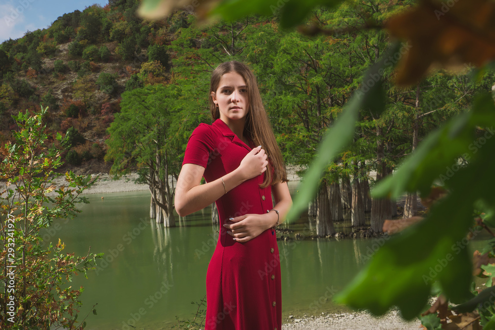 a beautiful, young brown-haired woman in a red dress on the background of a morning lake with cypresses, a girl with a slender figure posing against nature a beautiful, young brown-haired woman in a red dress on the background of a morning lake with cypresses, a girl with a slender figure posing against nature