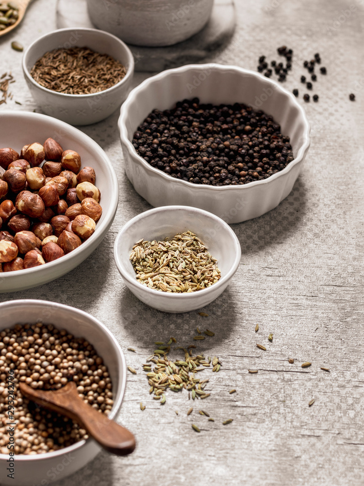 Assortment of spices, seeds and nuts in bowls on gray background Assortment of spices, seeds and nuts in bowls on gray background