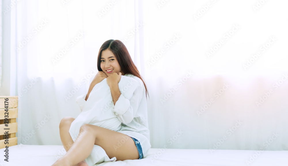 Cheerful young woman smile sitting on the white while hugging pillow in her arm at home. Joyful teenagers female long hair smiling while look at camera in the bedroom. Lifestyle concept. Cheerful young woman smile sitting on the white while hugging pillow in her arm at home. Joyful teenagers female long hair smiling while look at camera in the bedroom. Lifestyle concept.