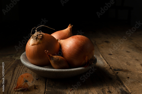 Brown onions and shallots in a stone bowl, on a rustic timber background. photo