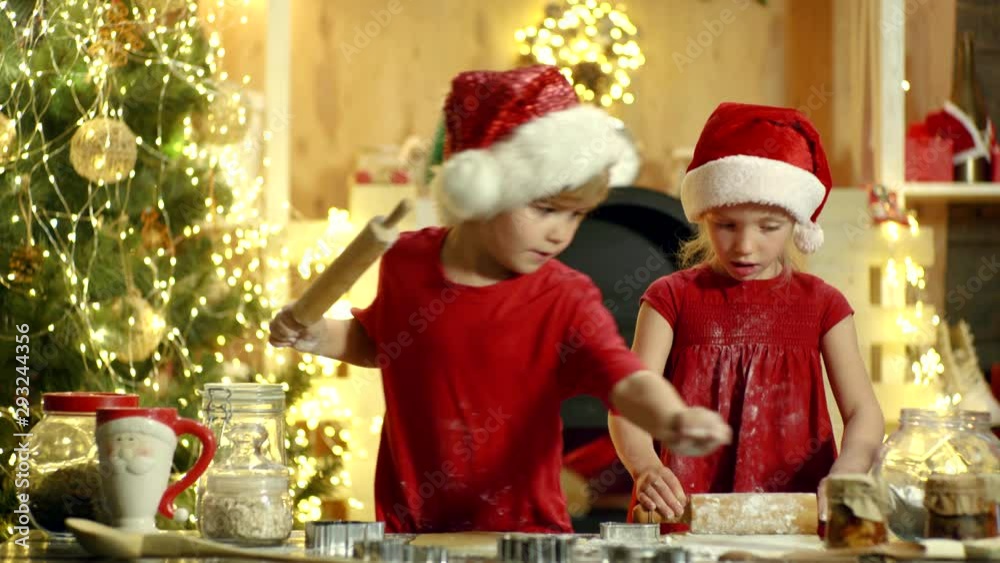 Christmas chef cook - children in Santa hat. Two children make gingerbread cookie for Santa against Christmas light background. Milk and cookies for Santa Claus. Christmas cookery.