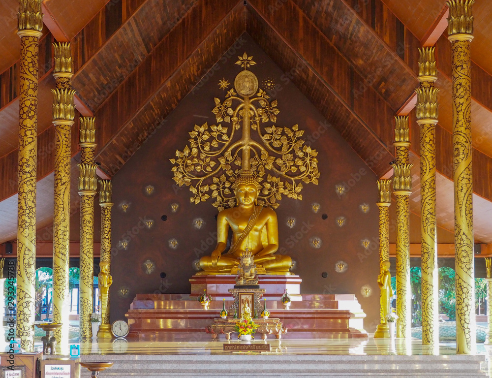 Ubon Ratchathani, TH - November 2, 2018: Big Golden Buddha Statue Sitting in the pavilion Behind him is a beautiful golden tree. At Sirinthon Wararam Phu Phrao Temple.