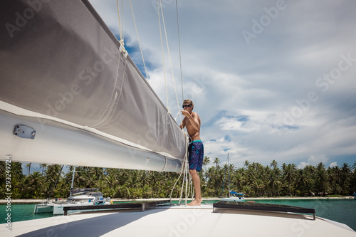 Canvas Print Young man preparing mainsail of catamaran