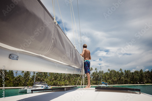 Картината върху платно Young man preparing mainsail of catamaran